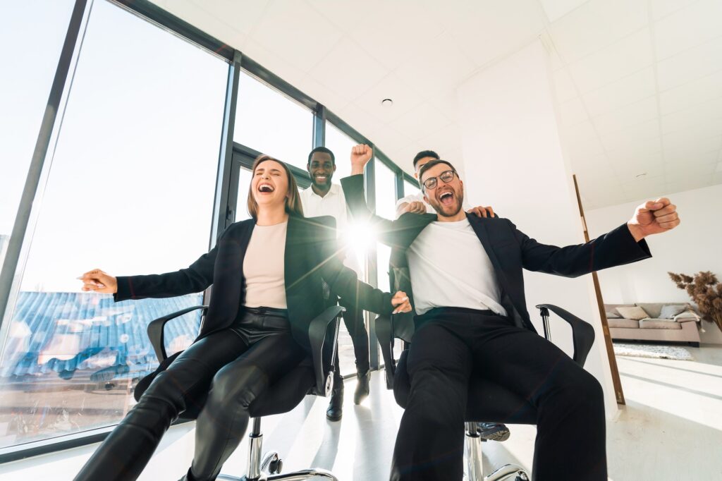 Office workers celebrate successful deal and ride on chairs